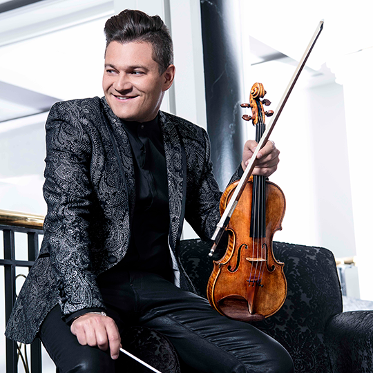 Alexandre Da Costa, a young man with dark hair wearing a shiny black jacket and holding a violin