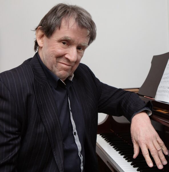 Man leaning on piano in black suit